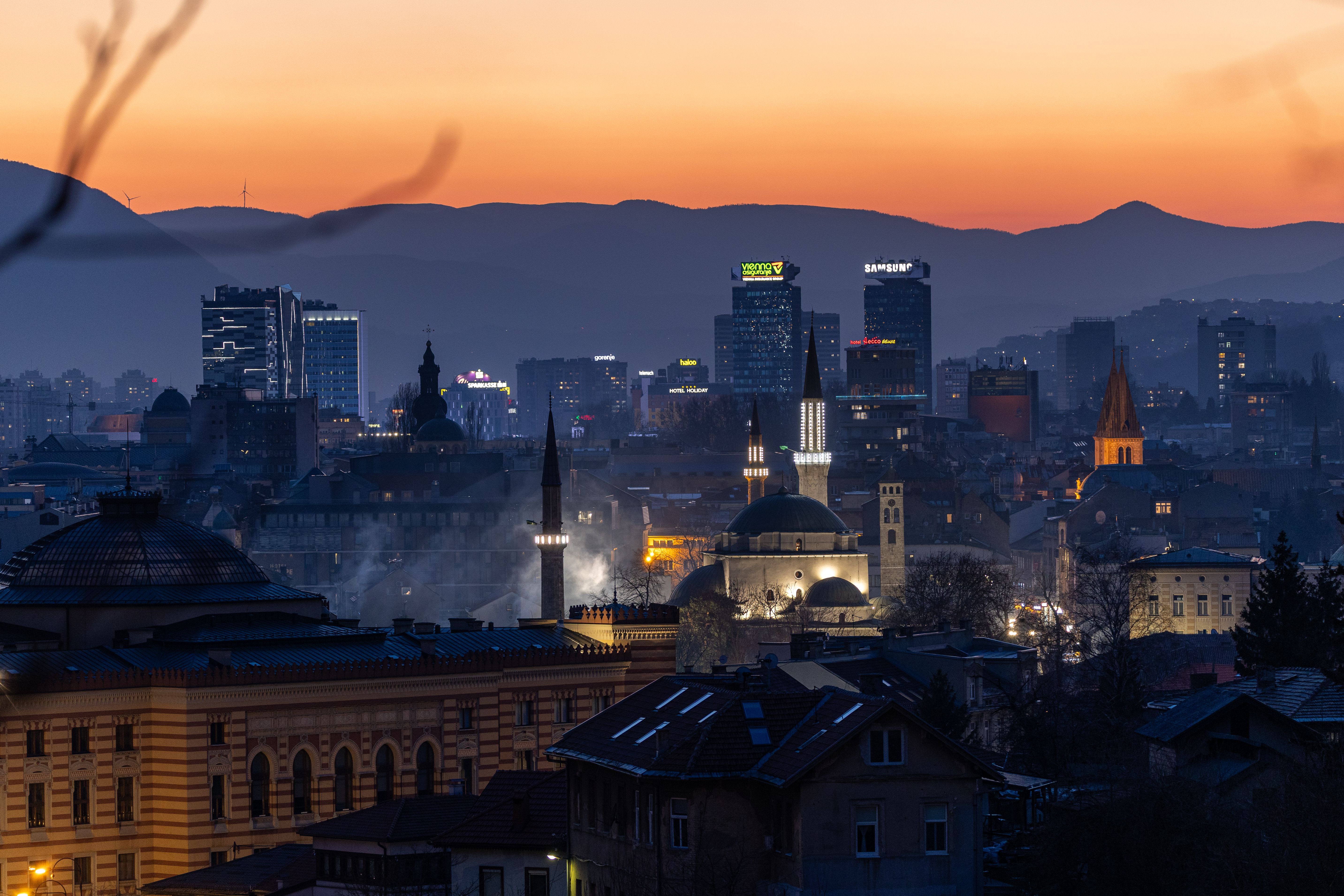 Panoramavy över Sarajevo i skymningen med stadens ljus och berg i bakgrunden.