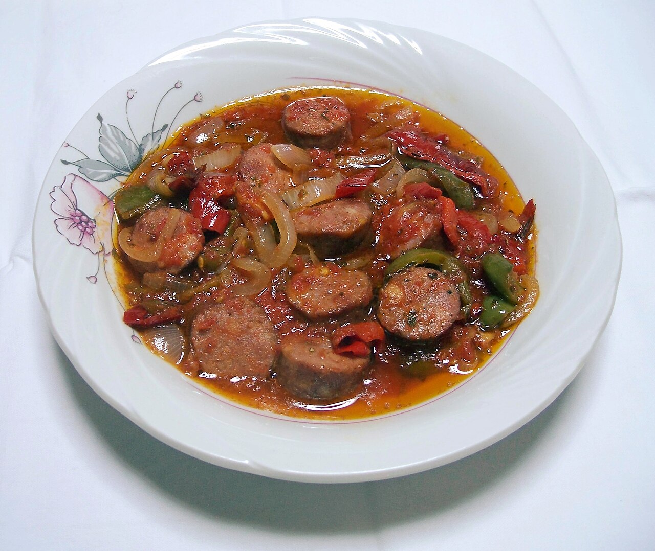 Spetzofai i en vit djup tallrik: skivad lantkorv med röd och grön paprika, lök och tomatsås.